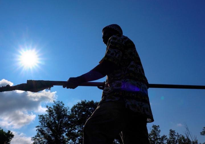 工作在与太阳和在他后的蓝天的一个领域的一个农夫的剪影。