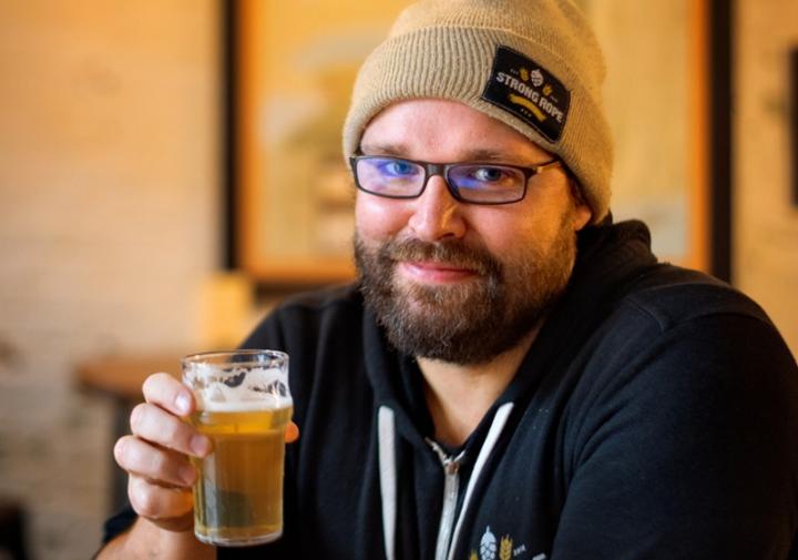 坐在桌上的一个人微笑对拿着啤酒的照相机